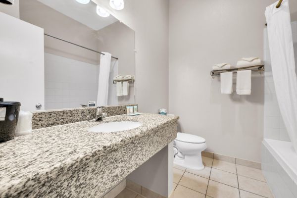 A clean bathroom with a granite countertop, sink, toilet, and tub. Towels are neatly arranged on a rack above the toilet.
