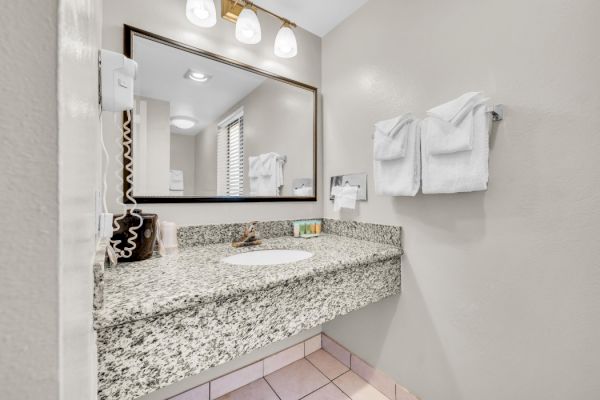 The image shows a bathroom with a granite countertop, a mounted mirror, wall-mounted hairdryer, and neatly folded towels on the wall.