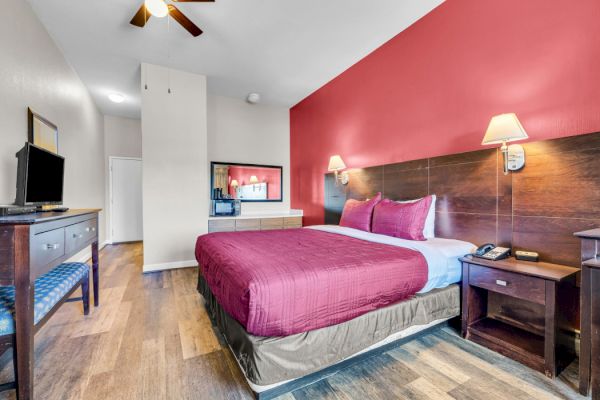 A hotel room with a bed, nightstands, TV, and dresser. The walls are red and white, with wooden flooring and a ceiling fan.